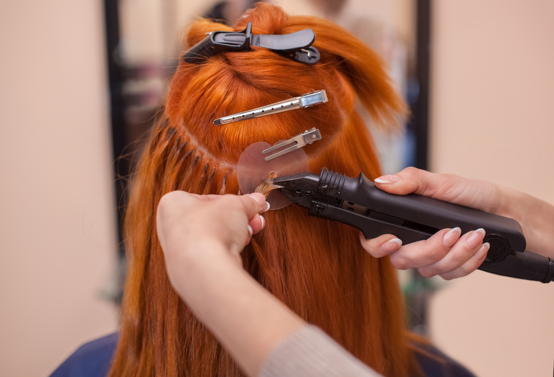 The hairdresser does hair extensions to a young, red-haired girl, in a beauty salon